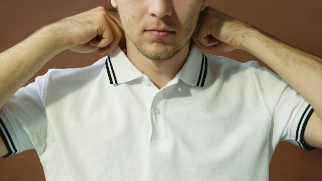 Close-up portrait of a man adjusting his polo shirt collar, artistic lighting.