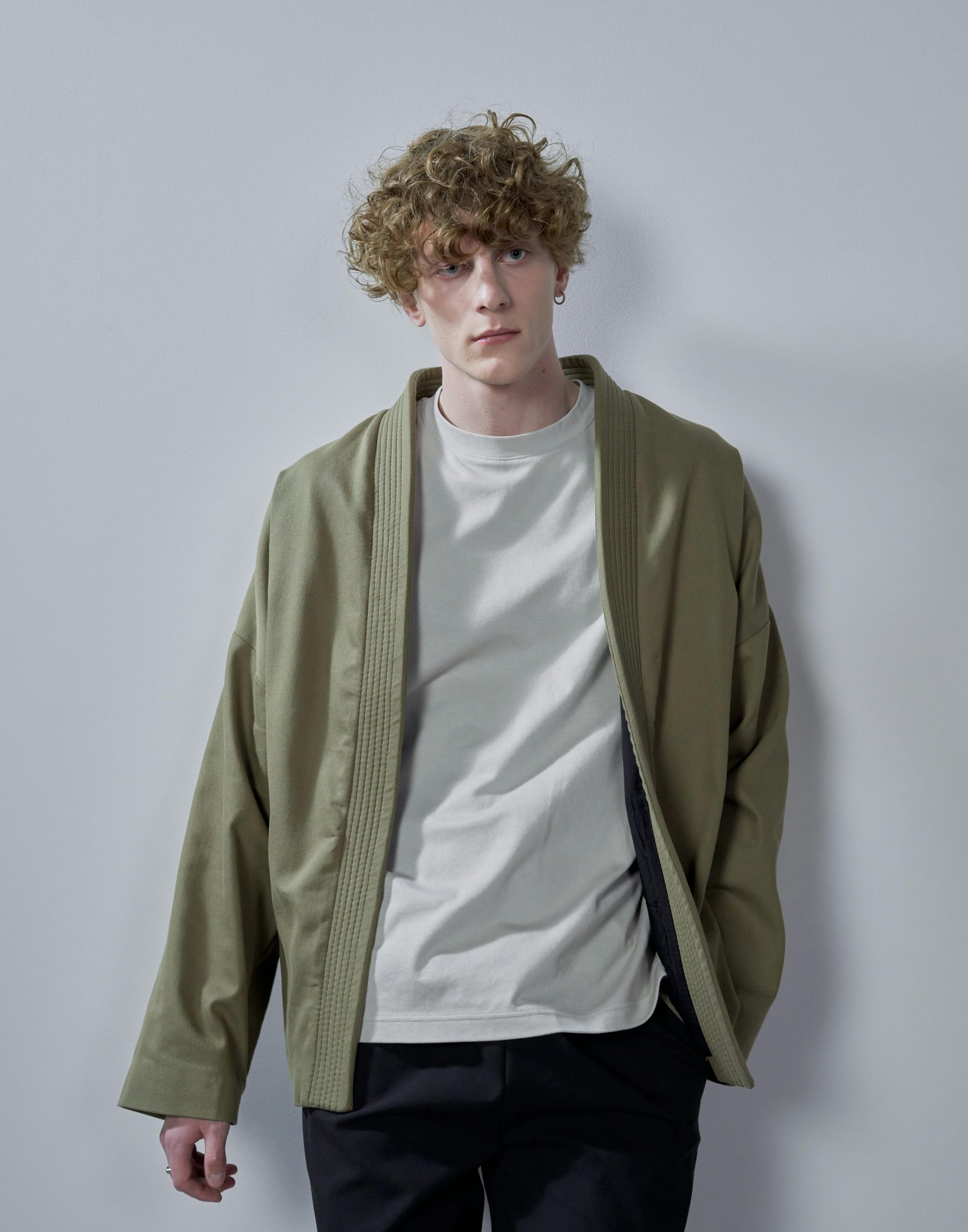 Studio portrait of a man with curly hair wearing casual attire against a gray background.